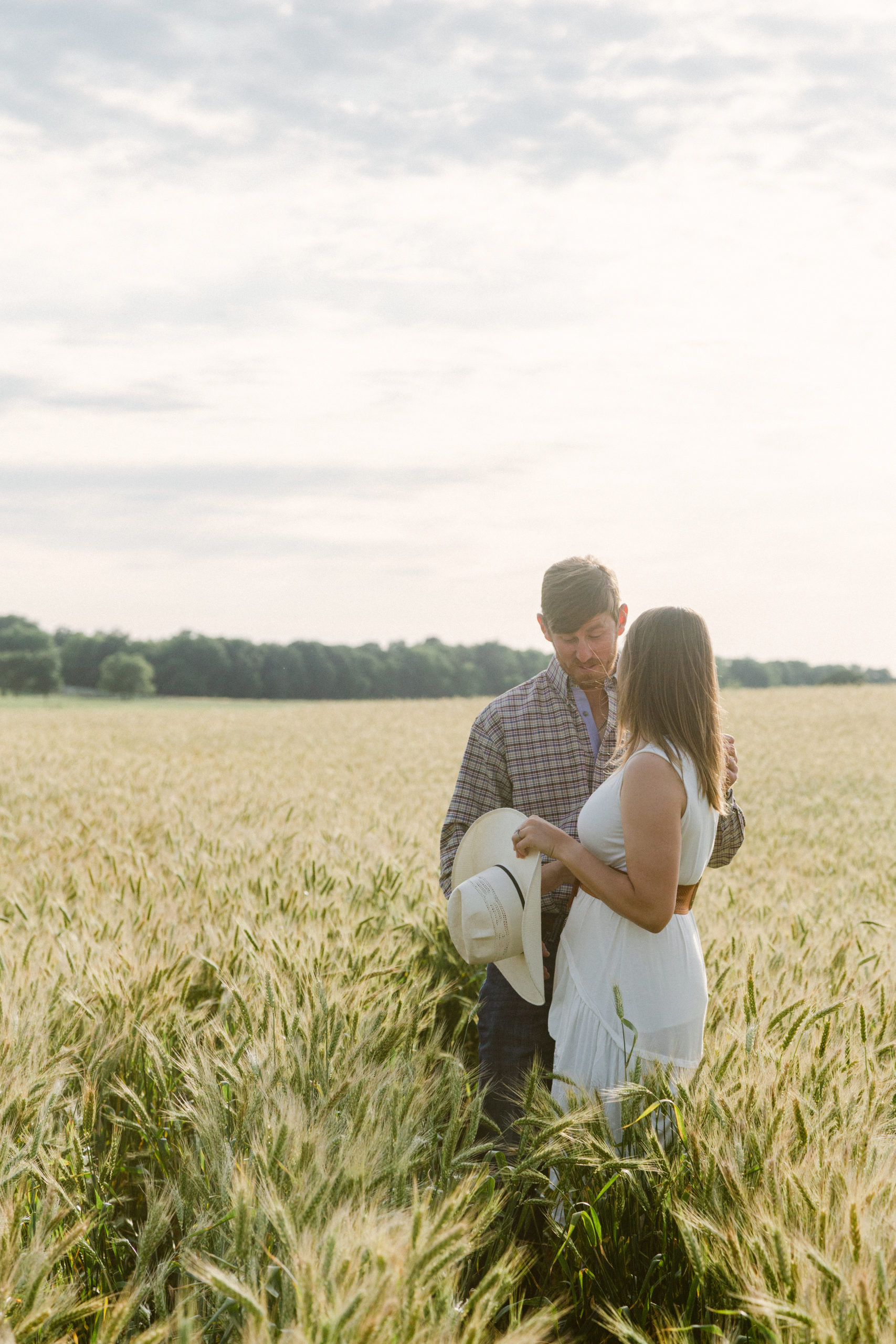 Kat holds Dillion's Cowboy hat while they stand in the wheat field