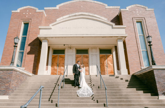 a wide angle shot of Meara and Joseph standing on the stairs outside their ceremony venue