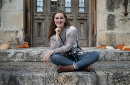 image of Samantha of Rae Allen photography. She is sitting cross-legged on the steps of an old building smiling at the camera