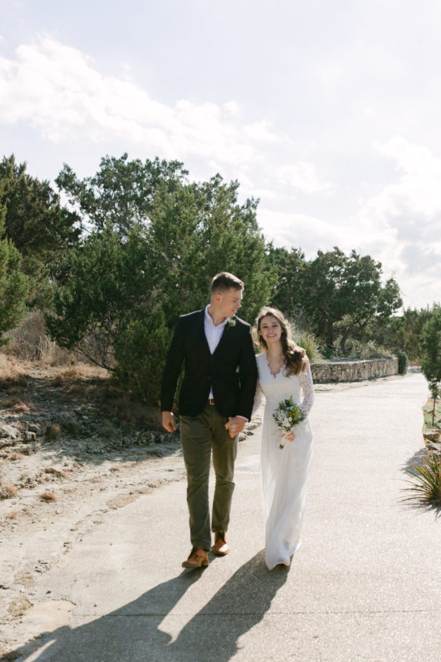 Henry looks at Elle as they walk towards the camera after just celebrating their marriage