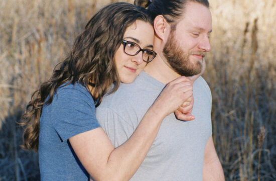 A Miller Spring Engagement Session, girl with dark hair and black glasses wraps herself around her fiancée's back as he looks at the ground | Rae Allen Photography