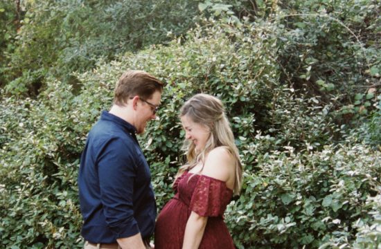 Hailee and her husband face each other and hold hands in the Carlene Bright aboretum gardens for her maternity session shoot by Rae Allen Photography