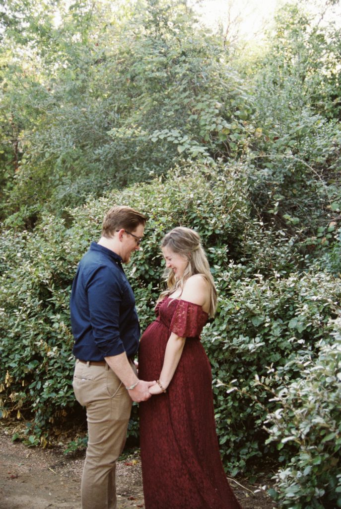 Hailee and her husband face each other and hold hands in the Carlene Bright aboretum gardens for her maternity session shoot by Rae Allen Photography