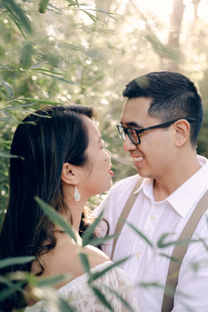 Tuyet and Jonathan stand in a bamboo forest looking at each other while surrounded by golden light during their engagment session at the Japanese Pagoda in Salado