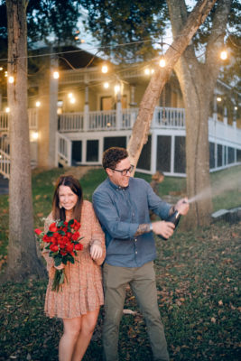 Kacie and Tyler celebrate their surprise proposal at Alexander's by opening a bottle of champagne. Holding red roses, Kacie laughs at Tyler pops the bottle.
