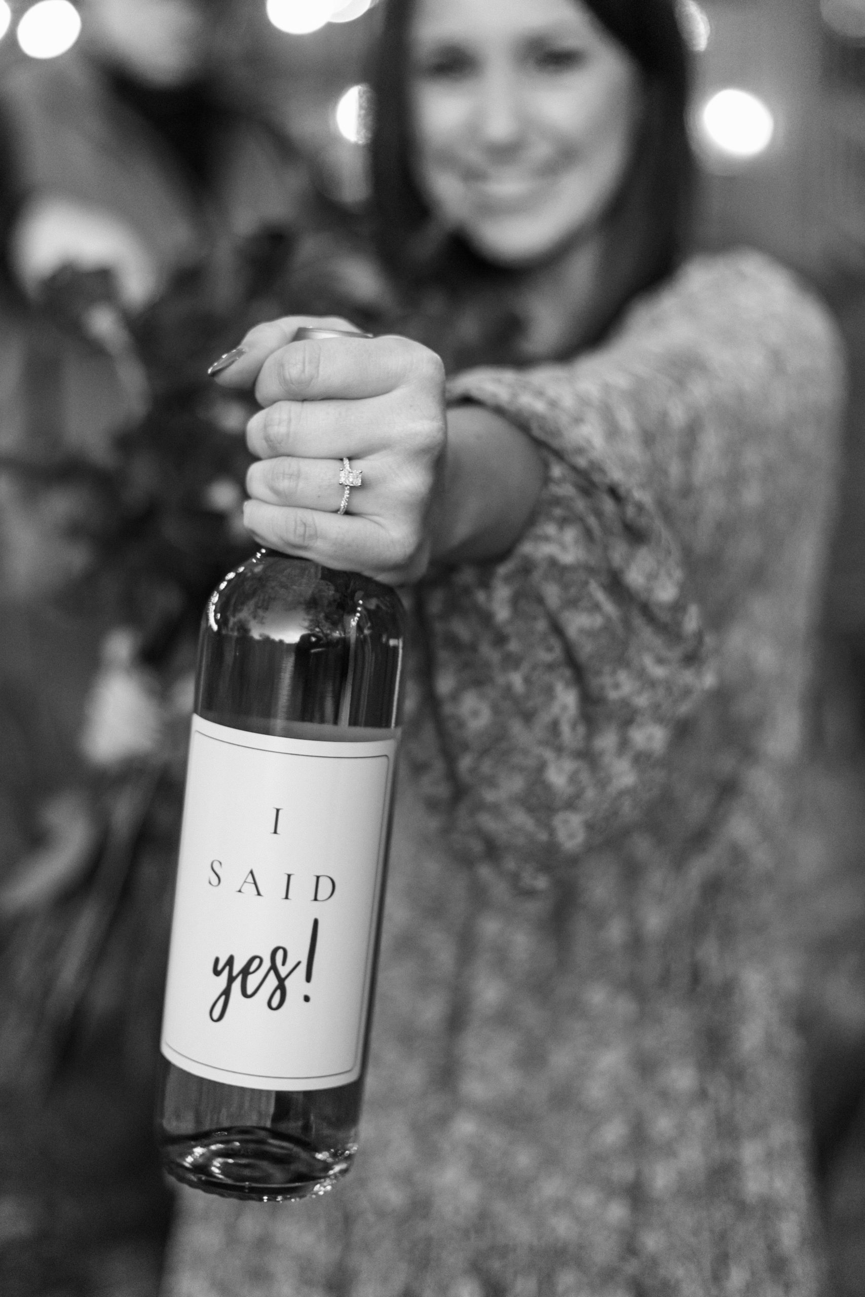 a black and white image of an of a wine bottle showcasing an engagement ring at a surprise proposal in Salado, TX This image is being used as an images on the investment page of the Rae Allen site.
