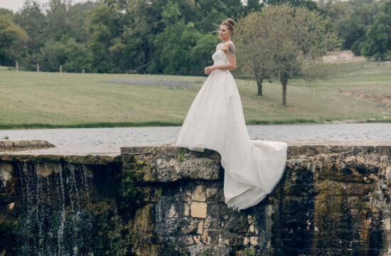 The is a feature image of a bridal session for Rae Allen Photography. It is a color image of a bride standing on s stone bridge overlooking water