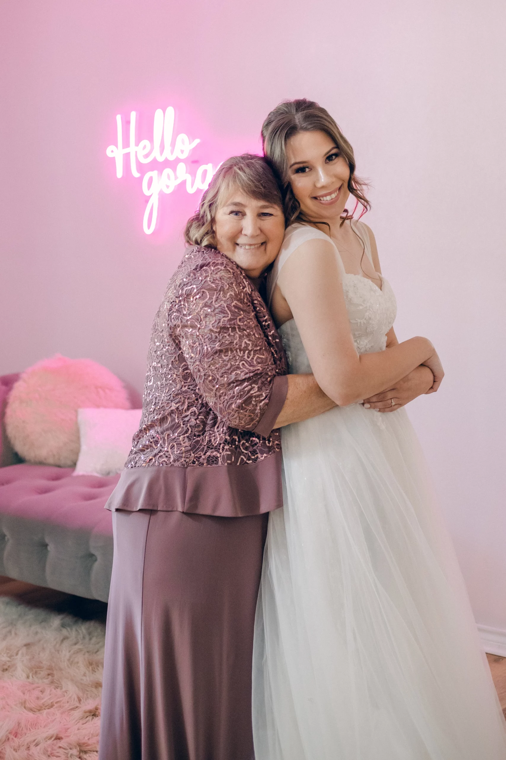 Clara's mother hugs her from behind as they smile at the camera