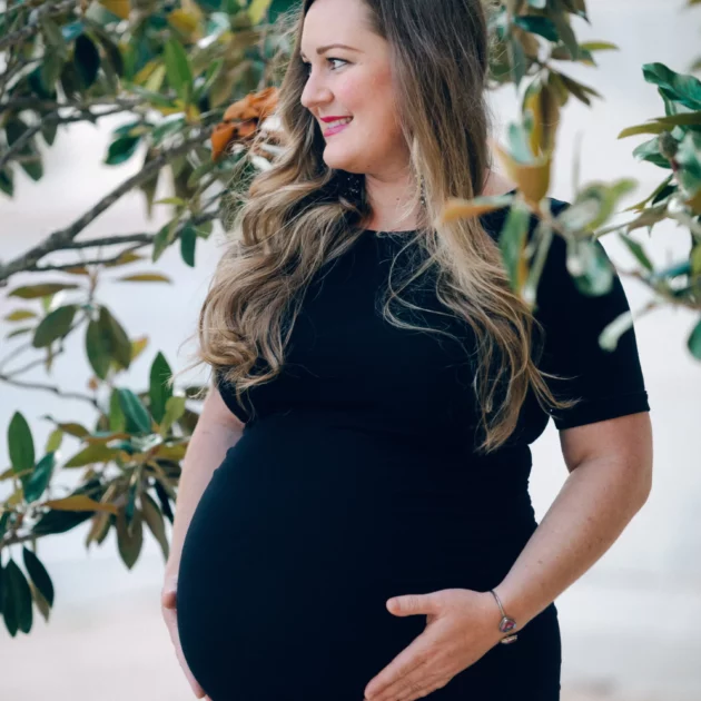 Jacqui holds her belly, while she stands next to a magnolia tree during her maternity session