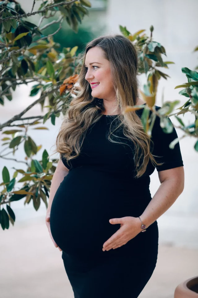 Jacqui holds her belly, while she stands next to a magnolia tree during her maternity session