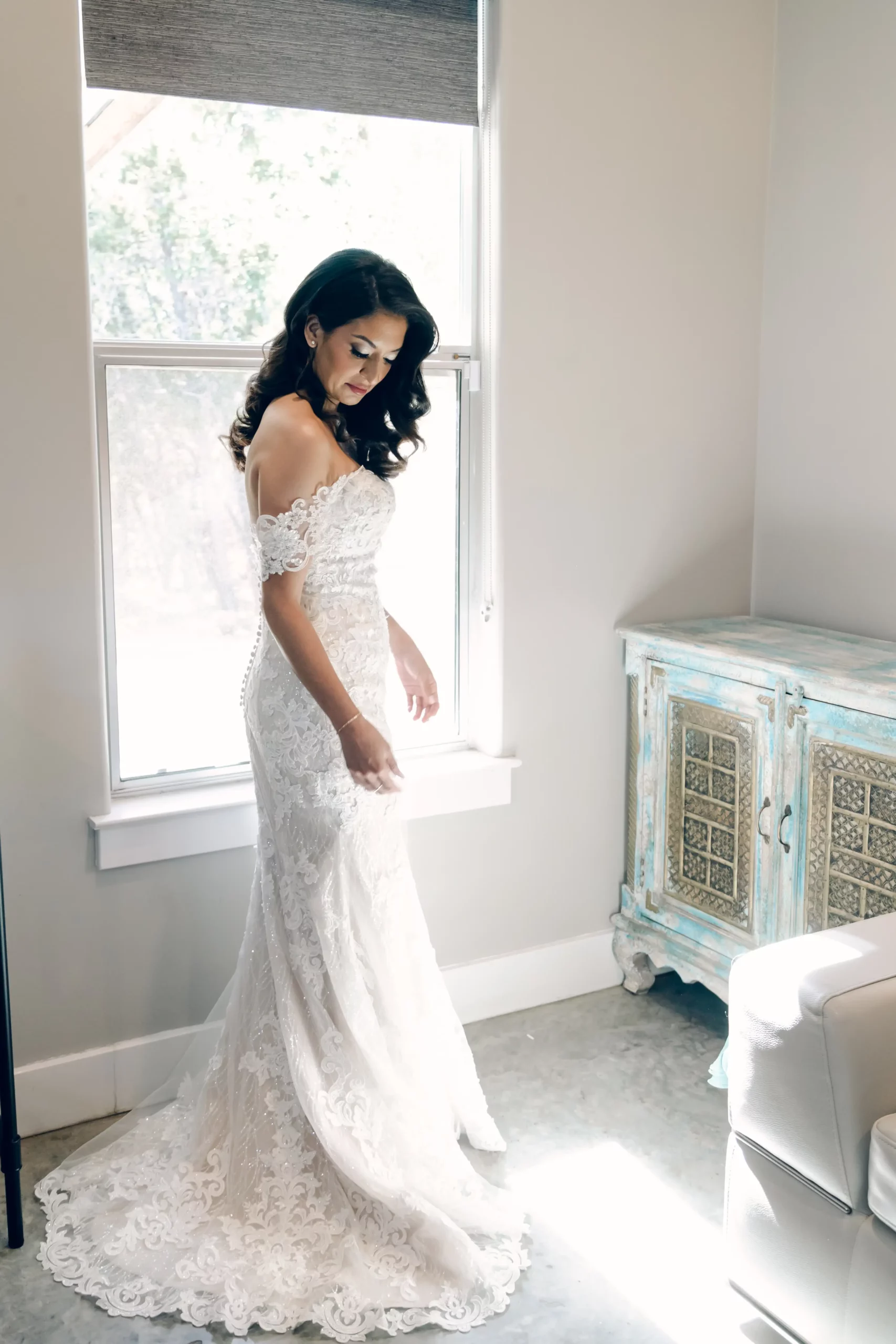 The bride stands in front of a window in her bridal suite waiting to getting married